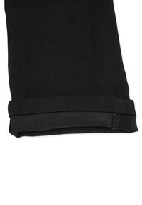 Mustat strakattomat housut, joissa on kestävä kangas ja sileä pinta, taitettu helma ja huomaamaton ompelu yksityiskohtia reunoilla.