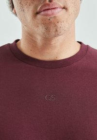 Bordowa bawełniana koszulka z okrągłym dekoltem. Posiada subtelne tonalne logo QS na piersi, gładką teksturę i dopasowany krój.