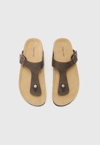 Brune thong sandaler med en suede-lignende sål, der har en overdel i mørkt læder og et metallisk spænde som accent. Blød tekstur, minimalistisk design.