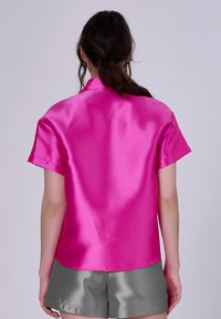 Chemise à col en satin rose à manches courtes, texture lisse et coupe régulière, associée à un short en satin gris pour un look décontracté.