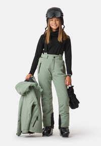 Skiausrüstung mit mintgrünen isolierten Hosen mit verstellbaren Trägern und Taschen, schwarzem Langarmoberteil, passender mintgrüner Jacke und schwarzem Helm.