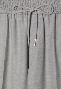 Graue Jogginghose aus weichem Stoff, mit elastischem Bund und Kordelzug mit Metallspitzen für eine verstellbare Passform. Glatte Textur.