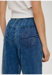 Modré džínové kalhoty s volným střihem, obsahující dvě zadní kapsy, viditelné švy a měkkou, opotřebovanou texturu.