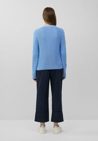Helles blauer Strickpullover mit gerippter Textur, kombiniert mit navyblauen weiten Hosen mit ausgestelltem Saum und weißen Plateausneakern.