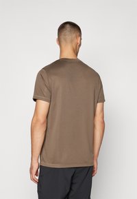 T-shirt marron à manches courtes, texture lisse, col rond, design ajusté et ourlets cousus. Porté avec un short foncé, vu de dos.