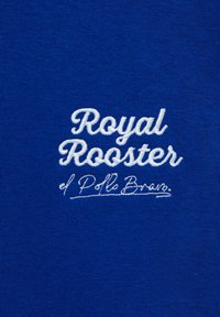 Blå tygdisplay med broderad text "Royal Rooster" och "d Polo Bran" i vit kursiv stil, med en texturerad finish.