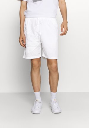 Shorts cargo blancs avec taille à cordon, dotés de poches latérales et d'un tissu texturé. Portés avec des baskets blanches et des chaussettes.