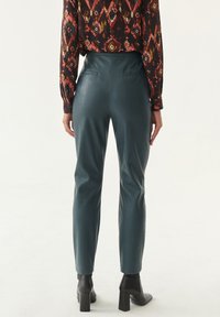 Pantaloni in pelle teal a vita alta con una texture liscia, design a gamba affusolata e orlo alla caviglia, abbinati a una maglietta a maniche lunghe con motivo.
