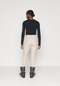 Zwarte lange mouw top gecombineerd met beige strakke broek en zwarte skiboots met witte accenten. Schone lijnen en minimalistisch ontwerp.