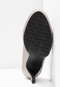 Semelle de chaussure à talon pailleté inclinée vers le haut, semelle en caoutchouc noir avec motif répétitif du nom de la marque « Tamaris ».