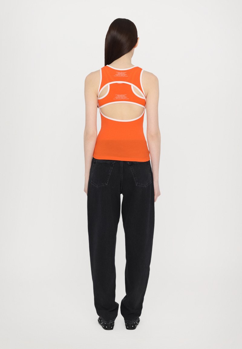 Top arancione senza maniche con dettagli bianchi e design con schiena scoperta; abbinato a jeans neri a vestibilità ampia e calzature con borchie.