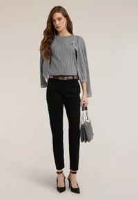 Suéter gris con costillas y tachuelas decorativas, pantalones negros a medida, tacones altos negros y bolso gris con detalles plateados.