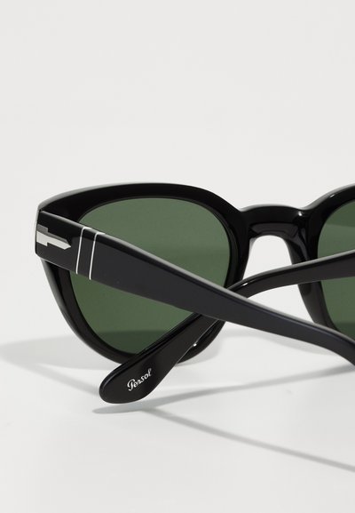Svarte solbriller med blank overflate, grønne linser, brede rammer og sølvdetalj på stengene. Merkenavnet "Persol" synlig på armen.