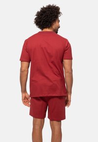 Punainen puuvillainen t-paita ja shortsit, joissa on lyhyet hihat, pyöreä kaula-aukko ja rento istuvuus. Sileä pinta, jossa on minimaalista yksityiskohtaa.