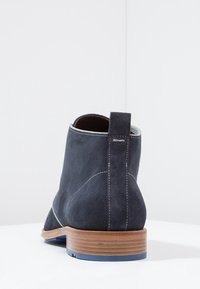 Bottine en daim gris avec un talon empilé marron, des coutures contrastées et une languette à l'arrière pour un enfilage facile.