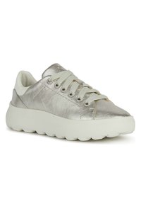 Zapatilla metálica plateada con cordones blancos, parte superior de cuero suave, puntera redondeada y suela blanca gruesa y texturizada. Diseño minimalista con acentos dorados.