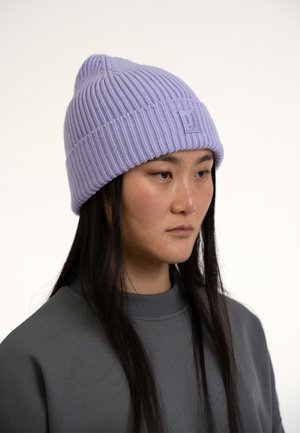 Paarse gebreide beanie met een geribbeld patroon, voorzien van een klein logo-opdruk. Draagt het met een grijs sweatshirt, haar gedeeltelijk zichtbaar.