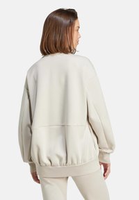 Krémový prehnaný sweatshirt vyrobený z mäkkého materiálu, s rebrovaným lemom a objemnými rukávmi. Hladká textúra, minimalistický dizajn.