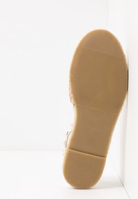 Semelle d'une sandale beige avec une semelle en caoutchouc texturée, taille 3, reposant verticalement contre une surface blanche.
