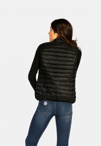 Gilet noir rembourré avec un motif matelassé, col montant et fermeture éclair. Porté par-dessus un haut à manches longues, assorti avec un jean ajusté.