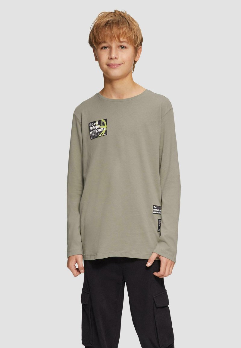 Langarm-T-Shirt aus leichtem olivgrünem Baumwollstoff mit einem quadratischen Grafikdesign auf der Brust und einem zusätzlichen Etikett am Saum.