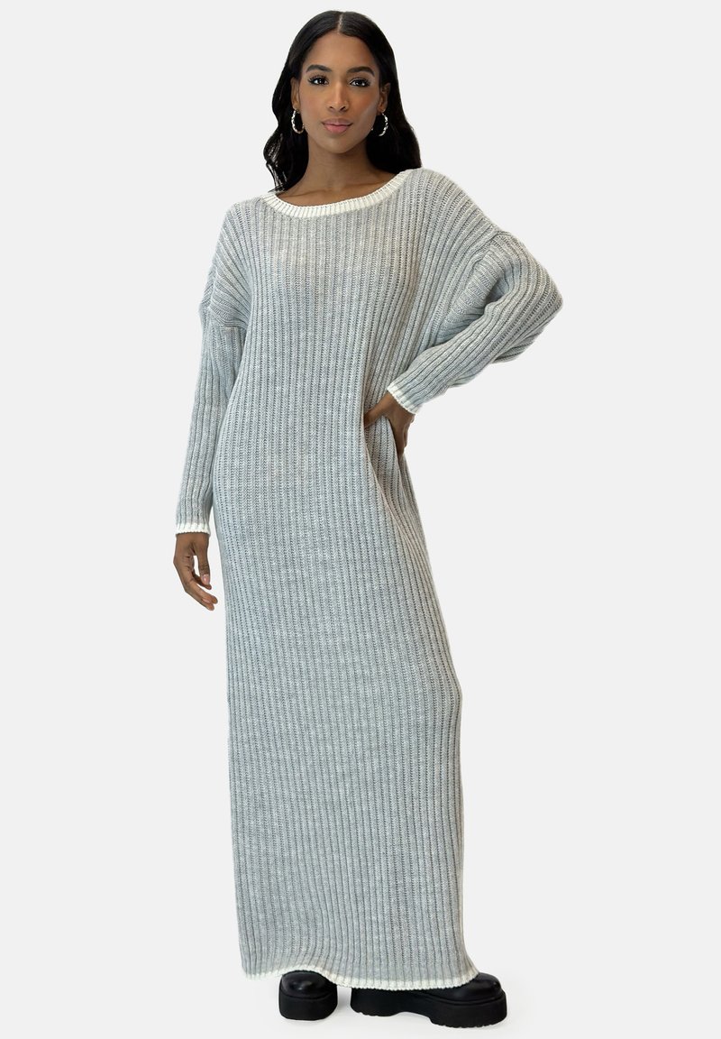 Abito maglione lungo a coste in grigio chiaro, con scollatura ampia e maniche scese, caratterizzato da una consistenza morbida e tasche laterali.