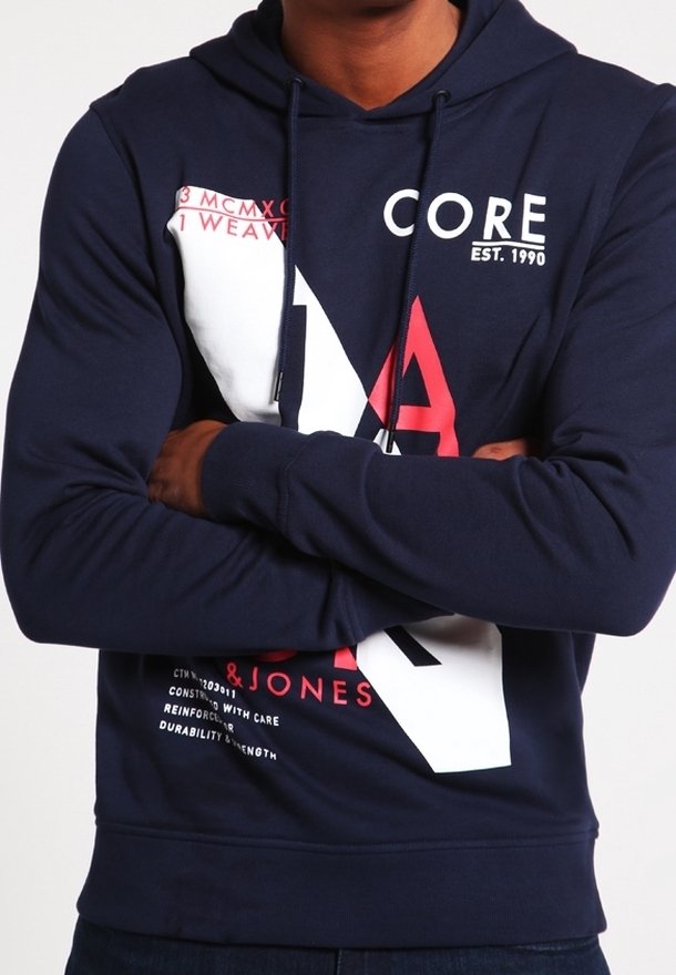 Personne portant un sweat à capuche bleu marine, les bras croisés, avec de grands textes graphiques blancs et rouges sur le devant.