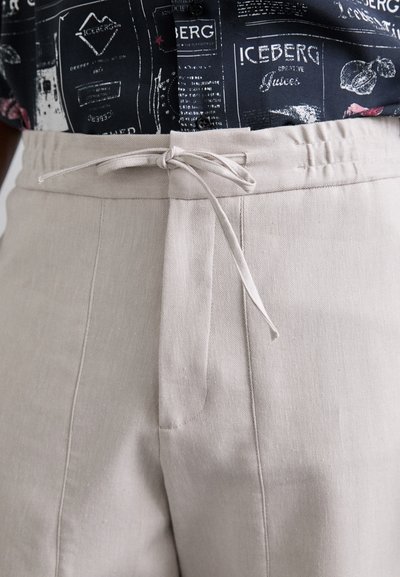 Béžové lněné kalhoty s pasem na šňůrku, s předními sklady a hladkou texturou. Dokončené herringbone vzorem.
