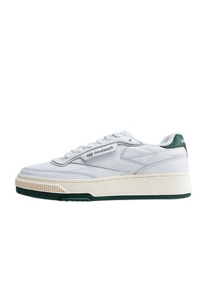 Sneaker bianca low-top Reebok con suola beige, dettagli verdi su suola e tallone, e logo laterale su sfondo semplice.