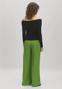 Schwarzes Off-Shoulder-Oberteil mit Raffung, kombiniert mit hochgeschnittenen, weiten grünen Hosen. Glatte Textur und lebendiger Farbkontrast.