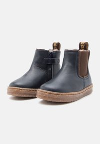 Botas de cuero hasta el tobillo en azul marino con paneles elásticos marrones, suelas marrones de textura rugosa, punta redondeada y tira para facilitar el uso.