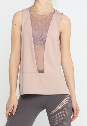 Frau trägt ein ärmelloses hellrosa Oberteil mit tiefem V-förmigem Mesh-Einsatz und dunkelgraue Leggings mit diagonalen Cut-out-Mustern.