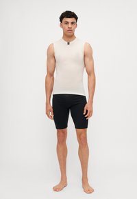 Haut ajusté sans manches beige et short de vélo noir en tissu extensible. Le haut présente une petite étiquette de marque au niveau du cou.