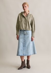 Kariertes grünes Hemd mit Kapuze, tailliert, kombiniert mit einem hellblauen Jeansrock und braunen Ankle Boots. Sichtbare glatte Texturen.