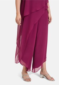 Pantalons en chiffon cramoisi superposés avec un design asymétrique, associés à des sandales à brides argentées avec des talons blocs et des accents en strass.