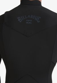 Traje de neopreno negro que presenta un collar alto, costuras cosidas y un logo de Billabong en gris oscuro en la parte superior de la espalda.