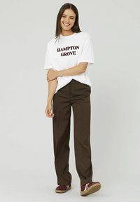 T-shirt blanche avec "HAMPTON GROVE" imprimé en bordeaux, associée à un pantalon large à rayures brunes et des baskets bordeaux.