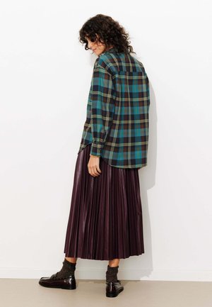 Chemise à carreaux bleu, vert et noir ; manches longues ; portée avec une jupe plissée d'un bourgogne profond ; chaussures brillantes ; chaussettes marron texturées.