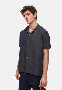 Camisa de lino de manga corta en azul oscuro con cuello con muesca, botones en la parte delantera y un corte relajado. Presenta una textura sutil y un ligero brillo.