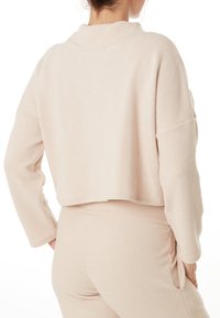 Lichtroze, gestructureerde, korte trui met een brede kraag en verlaagde schouders; gecombineerd met bijpassende, aansluitende broek. Beide hebben een ribbelontwerp.