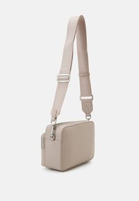 Borsa rettangolare beige con finitura in pelle liscia, hardware in argento e una tracolla regolabile con un motivo sottile. Comparti con zip visibili.