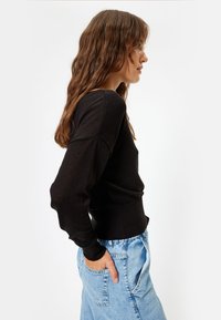 Schwarzes Langarmoberteil mit gerippter Textur, tailliertem Schnitt und überschnittenen Schultern, kombiniert mit hellblauen High-Waist-Jeans.