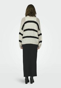 Crème oversized trui met zwarte strepen, gebreide textuur en lange mouwen, gecombineerd met een zwarte maxi-rok en zwarte blokhaklaarzen.