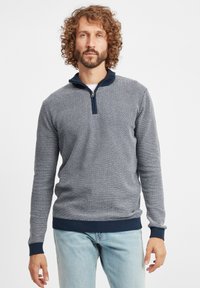Pulover tricotat în navy și alb cu un model texturat, guler cu fermoar și manșete și tiv elastic. Potrivit pentru îmbrăcăminte casual.