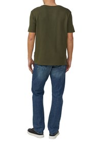 Oliwkowa koszula z krótkim rękawem o fakturowanej tkaninie, w połączeniu z niebieskimi dżinsami. Obuwie ma kontrastowy wzór.