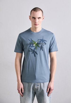 Herren T-Shirt mit kurzen Ärmeln in Hellblau mit einem grafischen Druck, der Pflanzen und den Text "Emporio Armani" in Schwarz zeigt. Weicher Stoff, normale Passform.