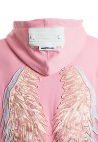 Sudadera con capucha rosa con diseños de alas bordados en tonos dorados y pasteles. Presenta una etiqueta blanca con el logo en la parte posterior del cuello.