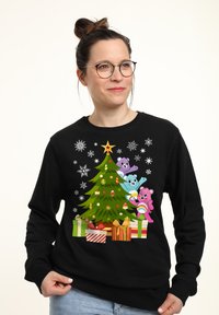 Sudadera negra con un gráfico colorido de un árbol de Navidad que presenta tres osos de dibujos animados y regalos, acentuado por copos de nieve y adornos.