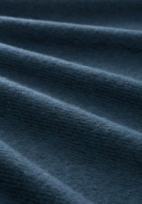 Dunkelblauer Stoff mit einer weichen, strukturierten Oberfläche, der subtile, unterschiedliche Rillen und Wellen aufweist, die durch das Drapieren des Materials entstehen.