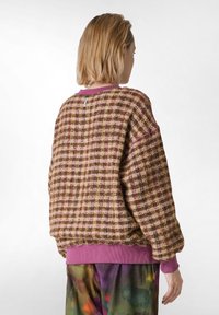 Pulover supradimensionat în carouri maro și roz, cu un material texturat, cu manșete și tiv ribonate de culoare mov. Include un detaliu cu eticheta pe spate.
